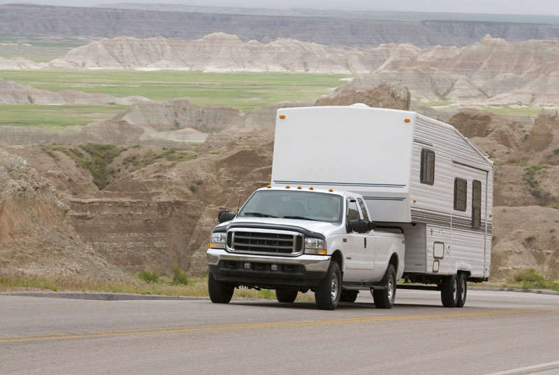 A white truck with a fifth wheel attached drives up a hill. 